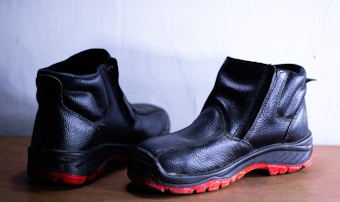 A pair of black leather shoes with a rugged design and distinct red soles placed against a light background. They appear sturdy and suitable for outdoor or work use.