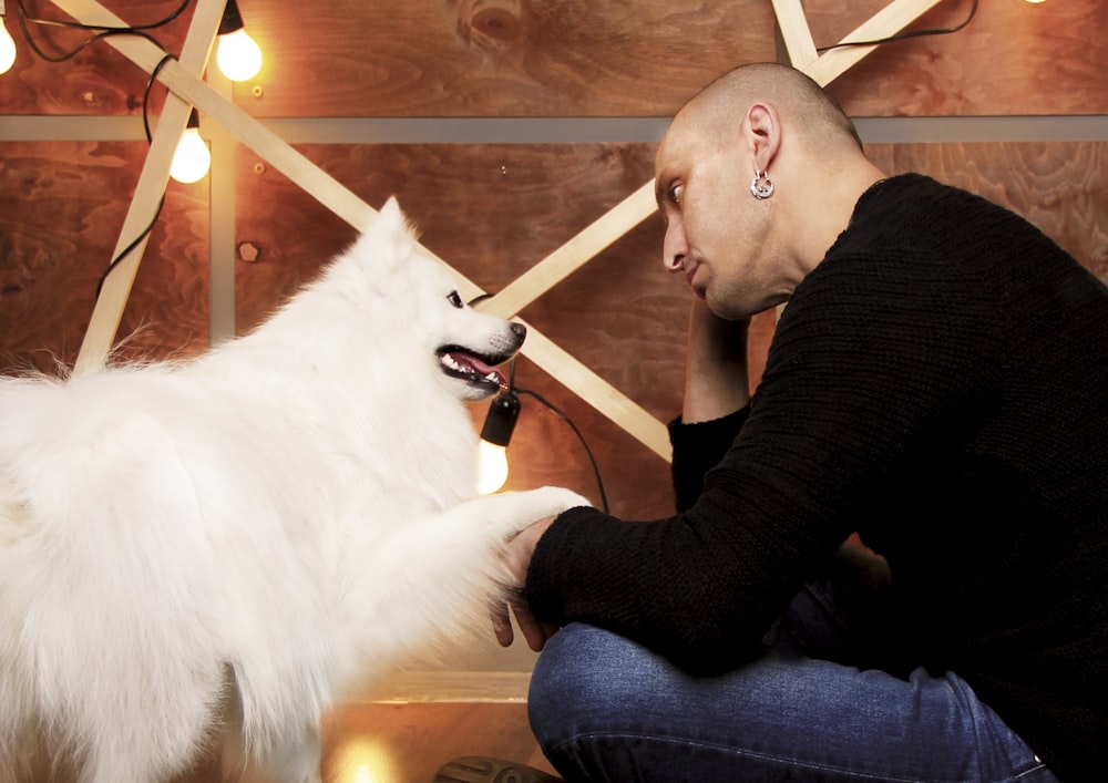 a man sitting on the floor petting a white dog