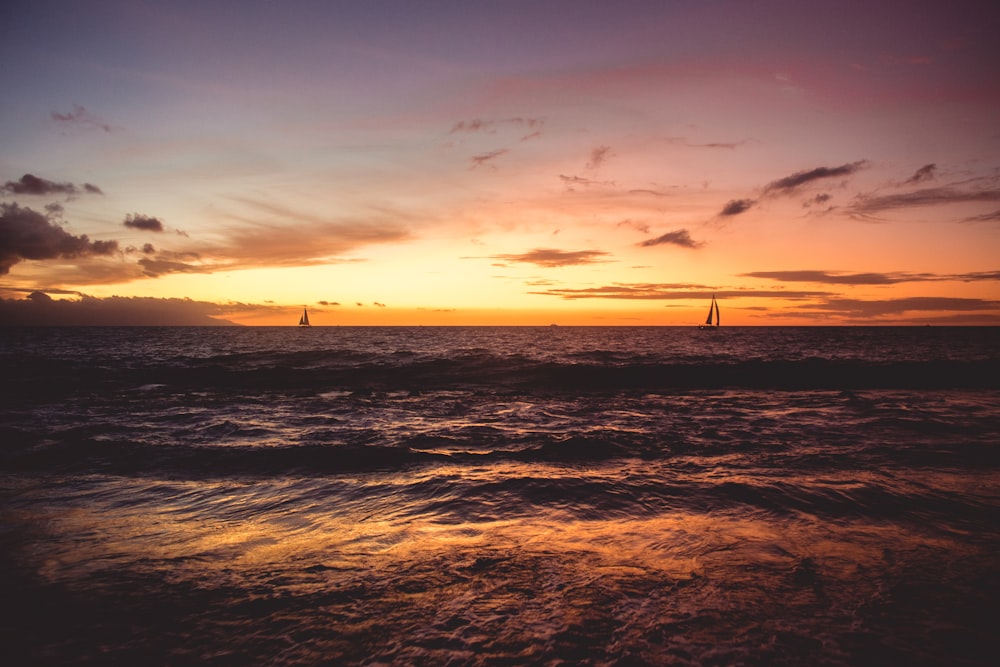 a sunset over the ocean with a sailboat in the distance