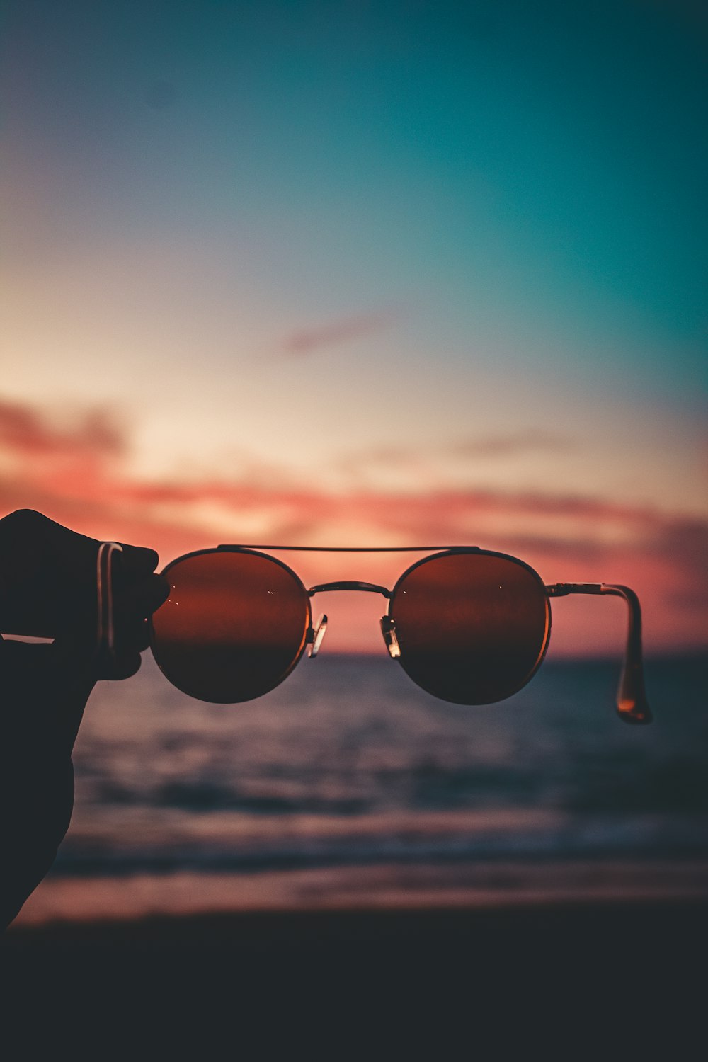 a person holding up a pair of sunglasses at the beach