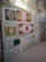 A wall displays a variety of decorative tiles arranged in a grid-like pattern. Each tile features intricate designs, including floral motifs and geometric patterns, in colors like red, yellow, brown, and blue. The wall itself is made of exposed brick and concrete, giving a rustic appearance.