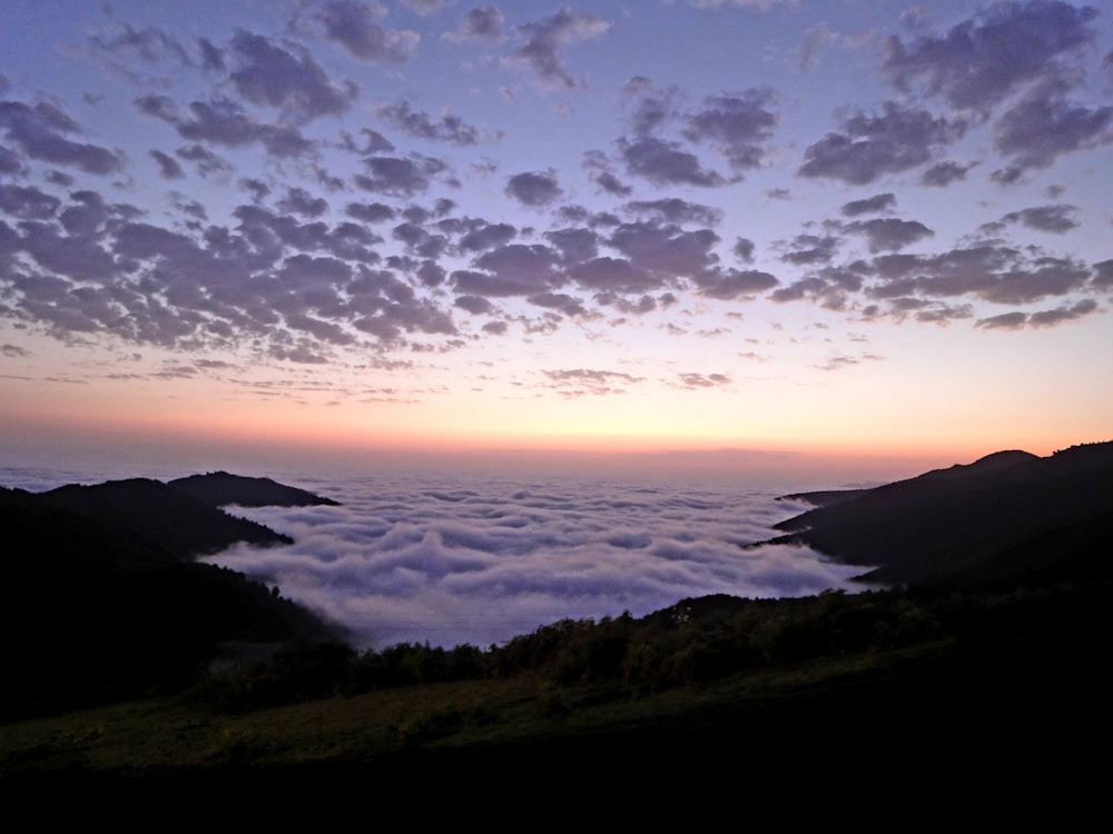 the sun is setting over the clouds in the mountains