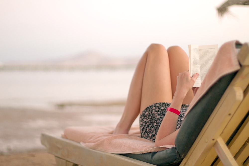 a woman laying on a beach chair reading a book