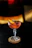 An elegant glass of orange-hued cocktail glowing softly against a dark bar backdrop.