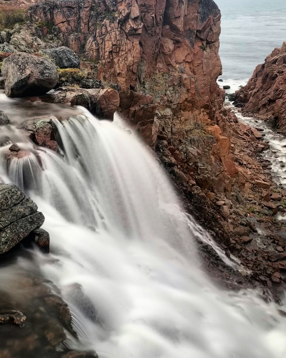 a large waterfall flowing over rocks into the ocean