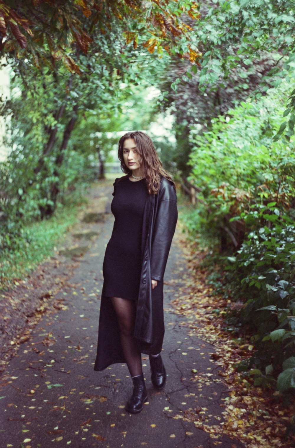 a woman in a black dress and coat is standing on a path