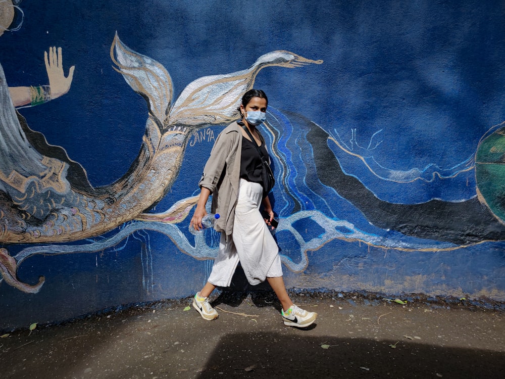 a woman wearing a face mask walks past a mural