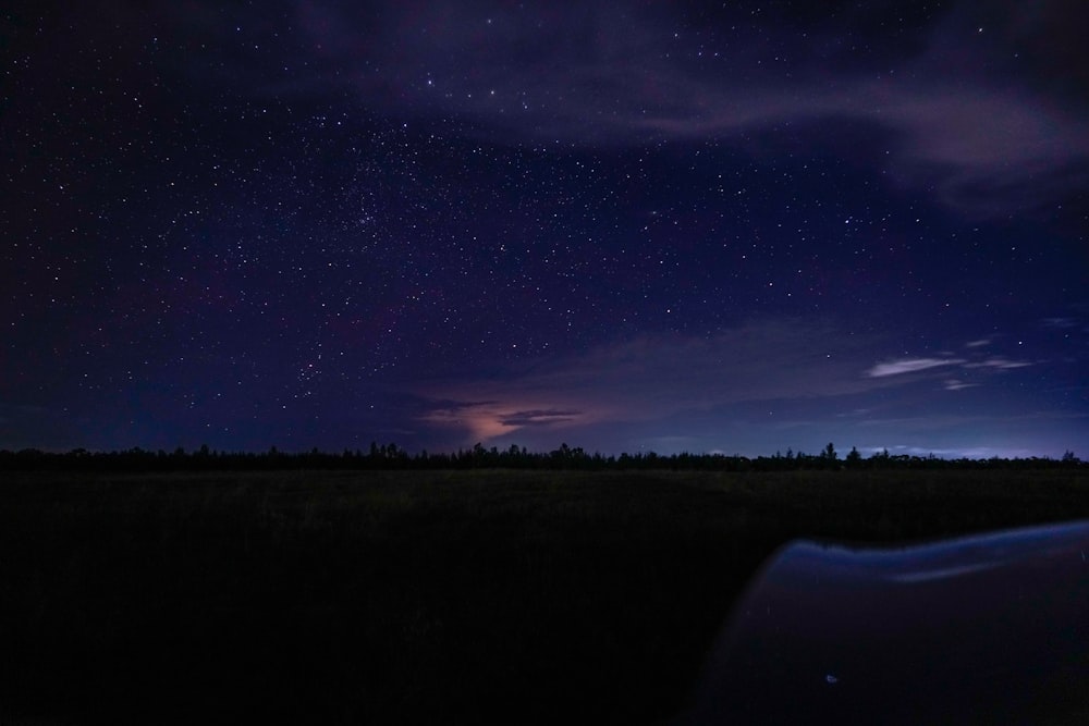 the night sky with stars and clouds above a field