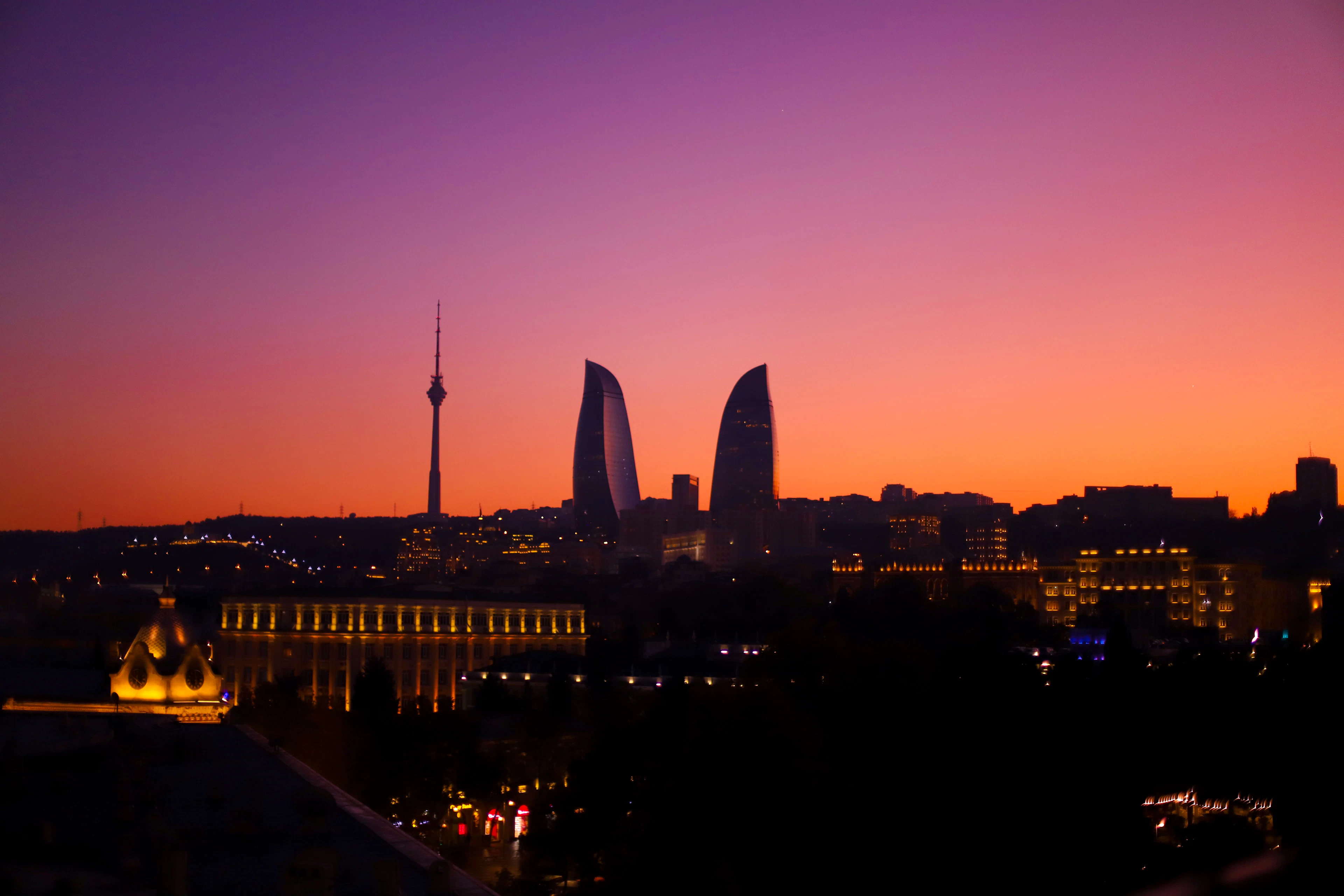 The Baku skyline in silhouette at sunset, with the TV tower and the Flame Towers against an orange and purple sky