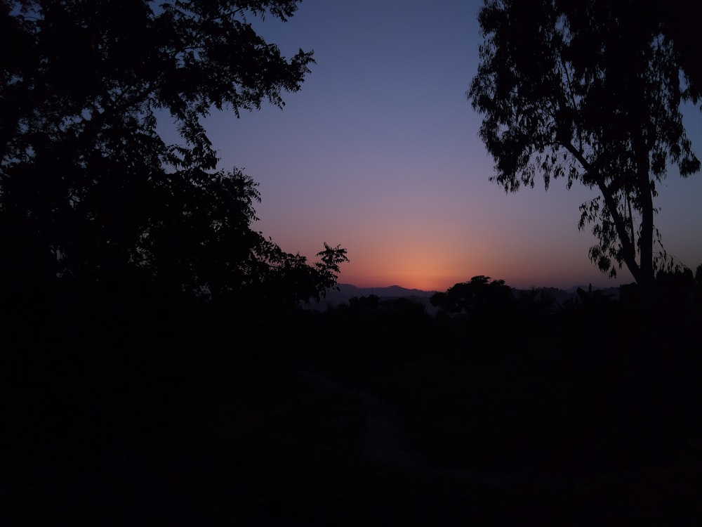 the sun is setting in the distance behind some trees