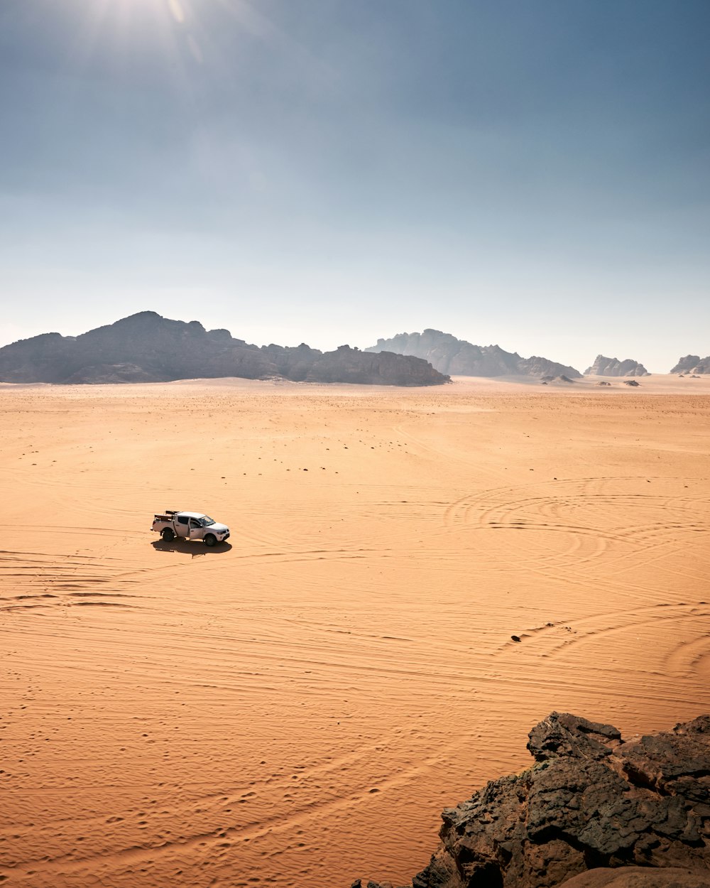 a vehicle driving through the desert with mountains in the background