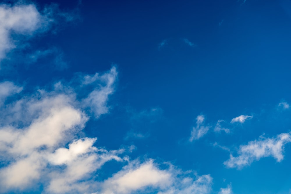um avião voando através de um céu azul com nuvens brancas