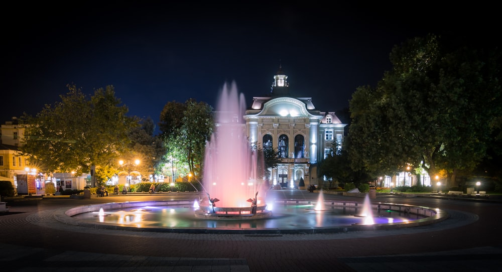 a fountain in front of a large building at night