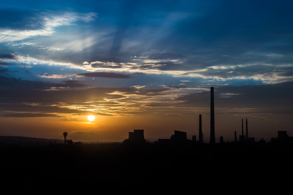 the sun is setting behind a factory with smoke stacks