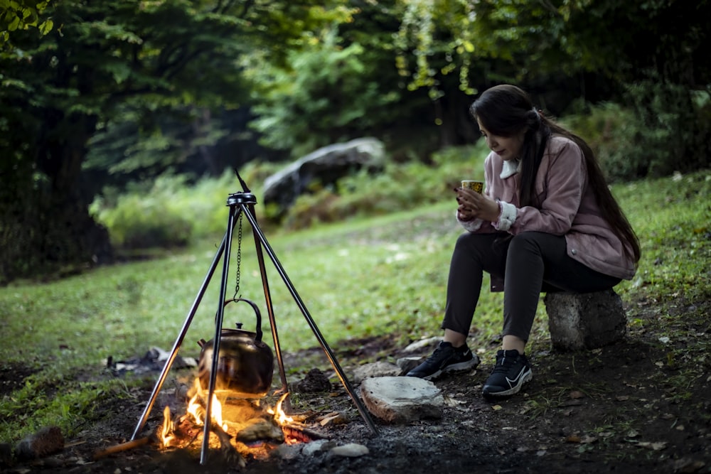a woman sitting next to a campfire looking at her cell phone