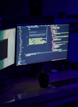 Close-up of a developer's hands typing code on a laptop surrounded by charts and analytics on dual monitors.