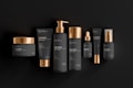 A collection of black and gold cosmetic containers arranged in a row. The set includes a jar, tubes, bottles with pumps, and a dropper bottle. Each item is designed with a matte black finish and shiny gold accents, giving a luxurious and elegant appearance. The products are labeled with the word 'cosmetic' and have simple, minimalistic typography.