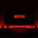 A television screen displays the Netflix logo in red against a black background. The room is dimly lit with a red glow possibly from LED backlighting behind the screen. Two speakers are positioned on either side of the TV set atop a minimalist entertainment center.