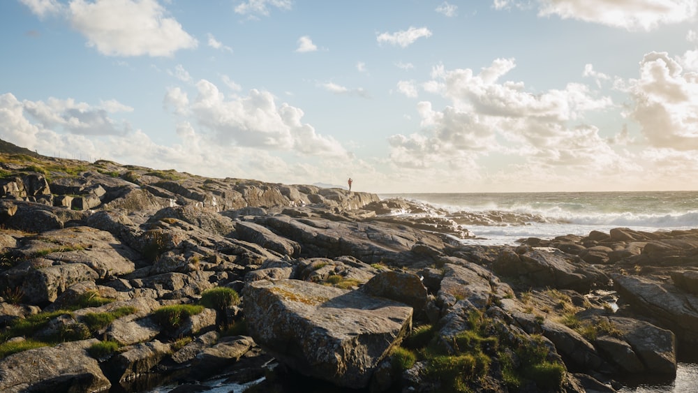 a person standing on a rocky beach next to the ocean