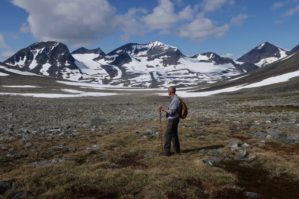 a man with a backpack standing in a field with mountains in the background