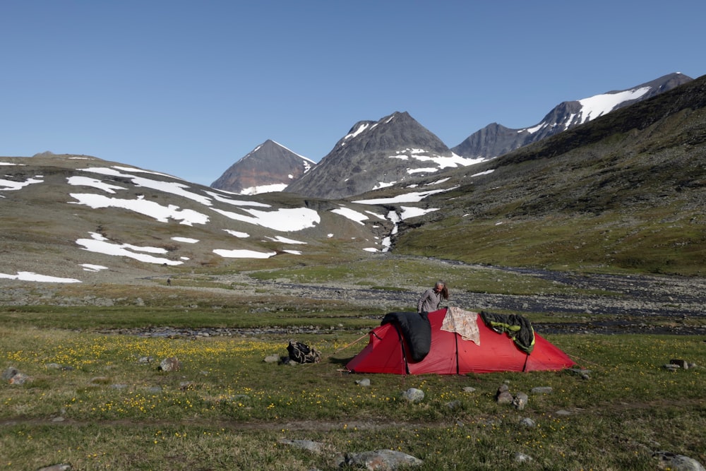 um homem de pé ao lado de uma tenda vermelha nas montanhas