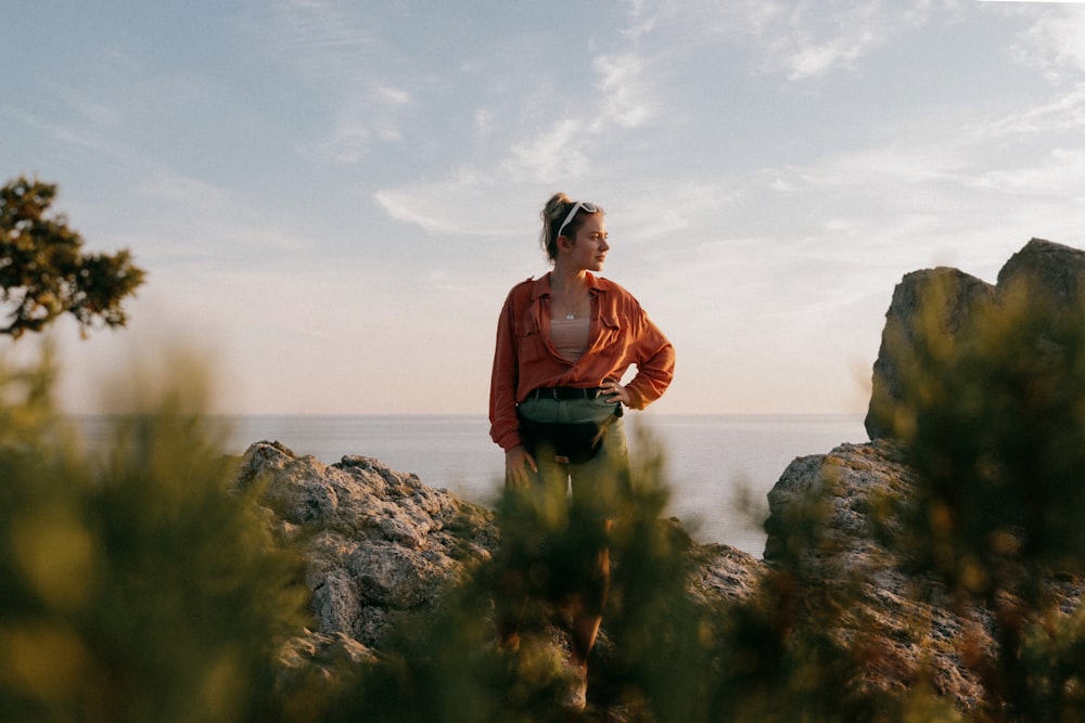 a woman standing on top of a rock next to the ocean