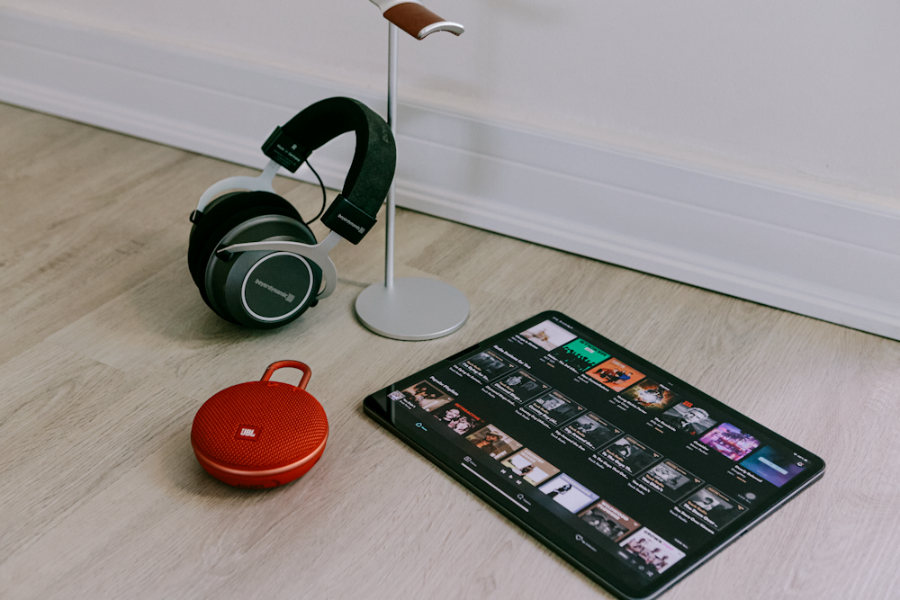 une paire d’écouteurs posée sur un plancher en bois à côté d’une tablette
