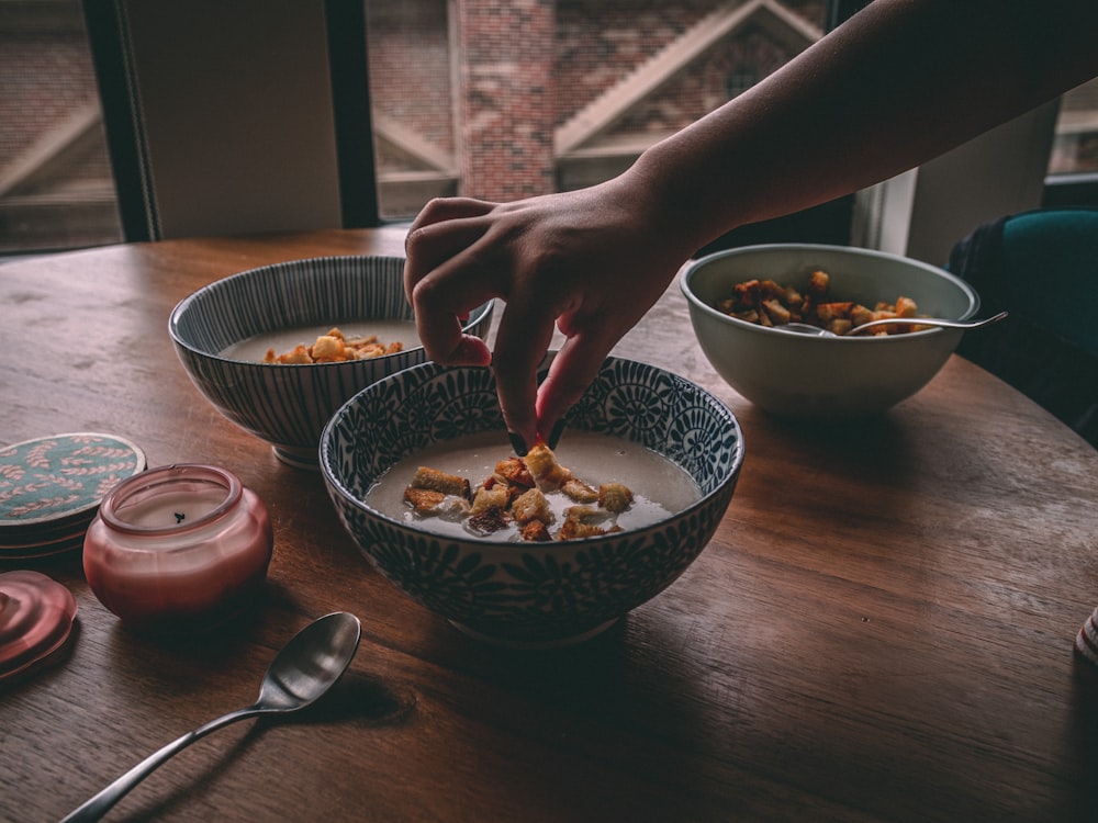 a person reaching for a spoon in a bowl of cereal