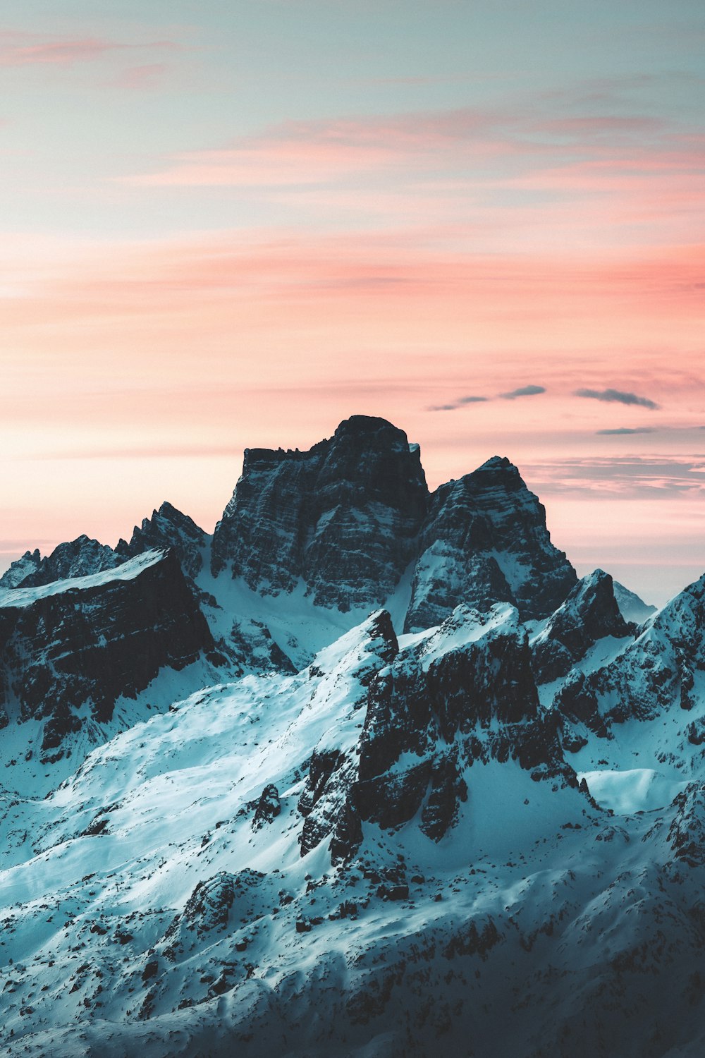 a group of mountains covered in snow under a pink sky