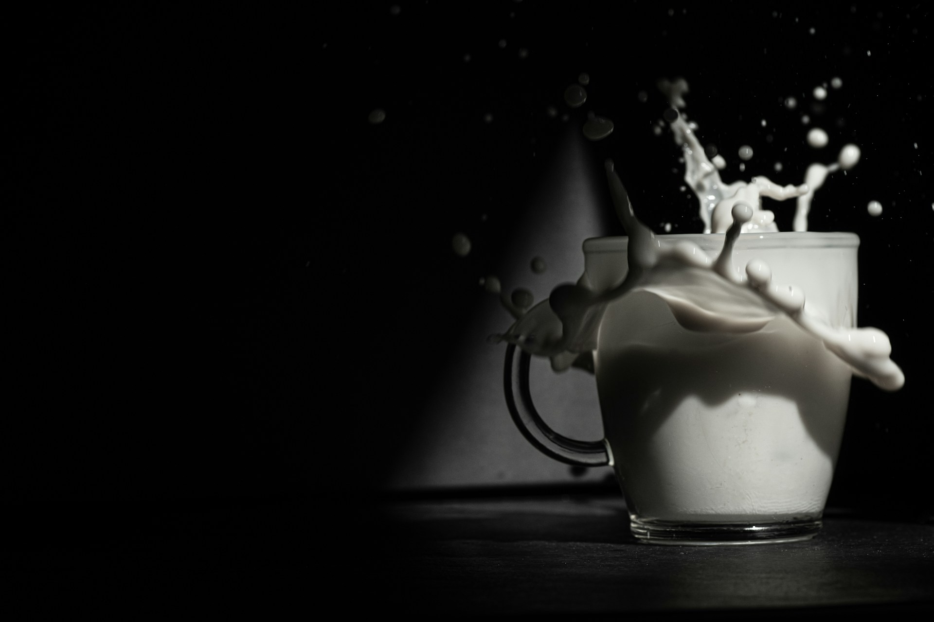 A cup is filled with milk as a splash emerges dramatically, creating dynamic droplets against a dark background.