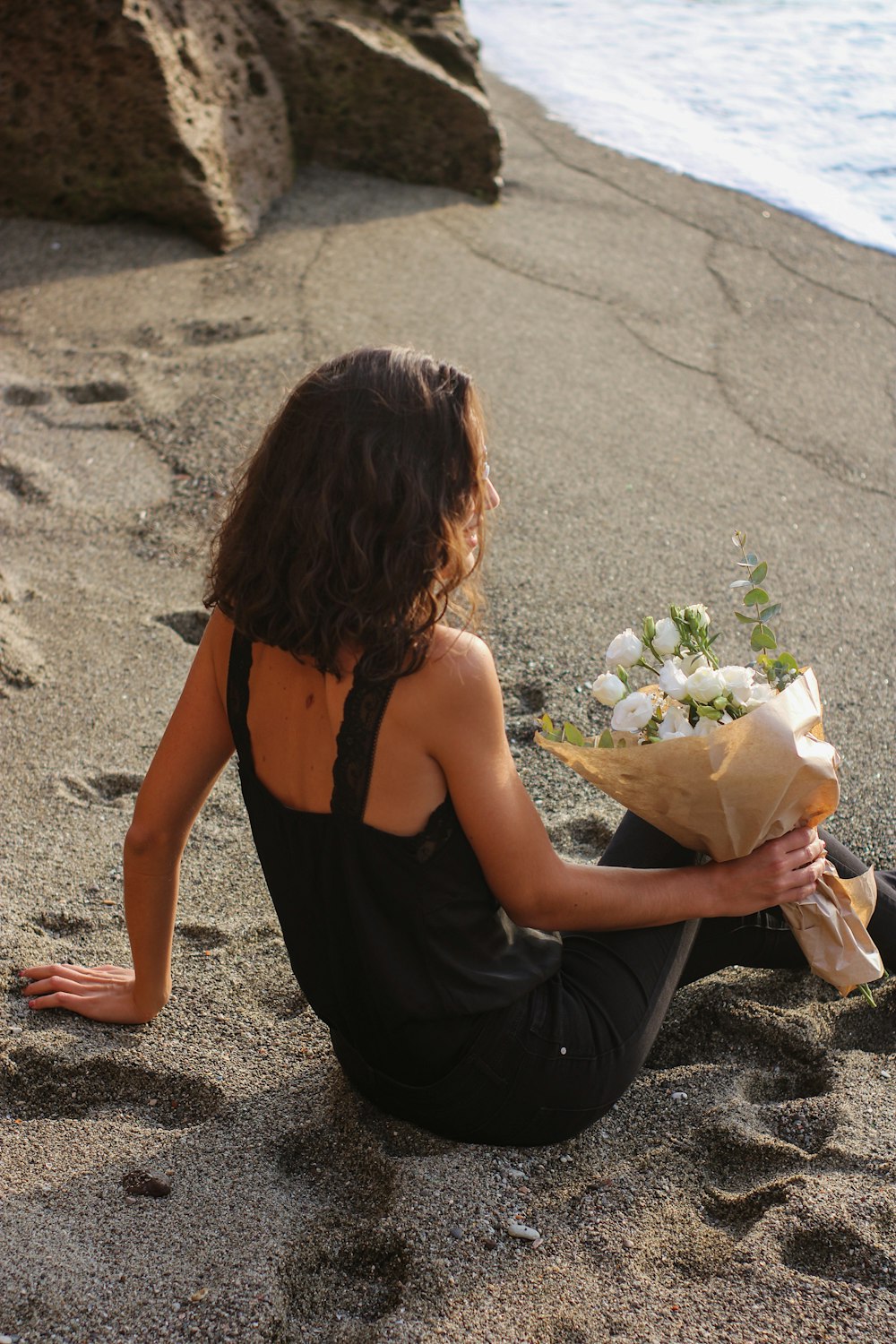 a woman sitting on a beach holding a bouquet of flowers