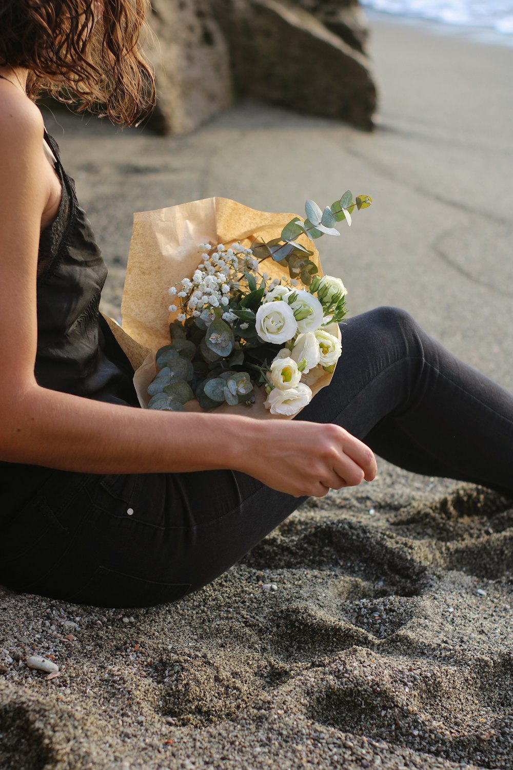 a woman sitting on the beach holding a bouquet of flowers