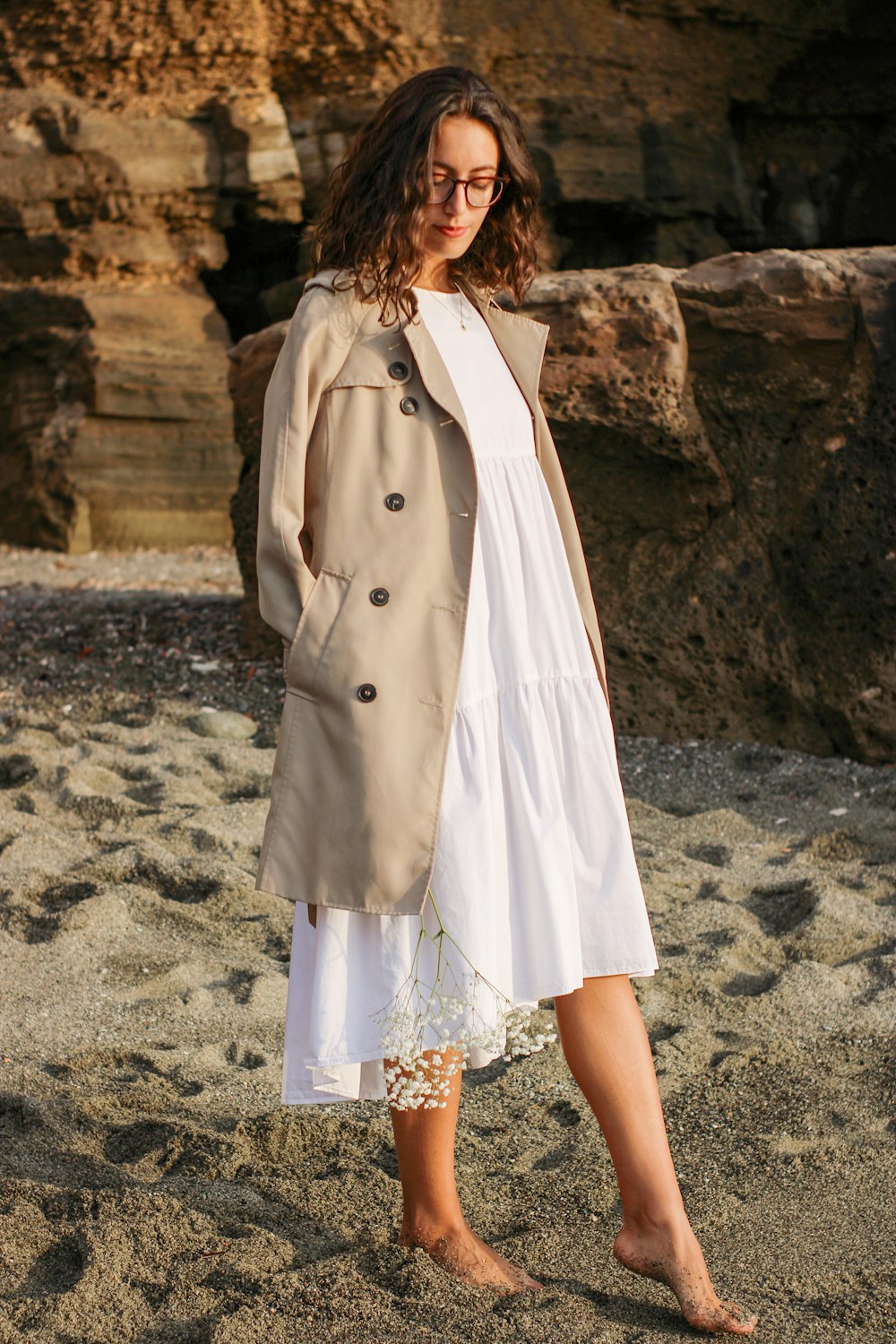 a woman in a trench coat standing on a beach