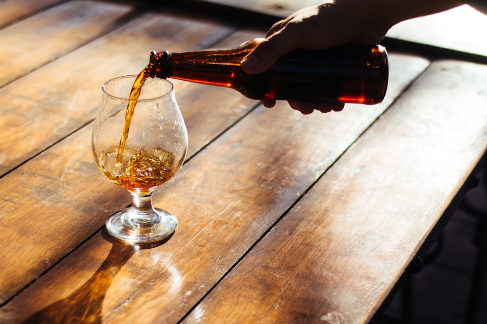 a person pours a glass of wine on a wooden table