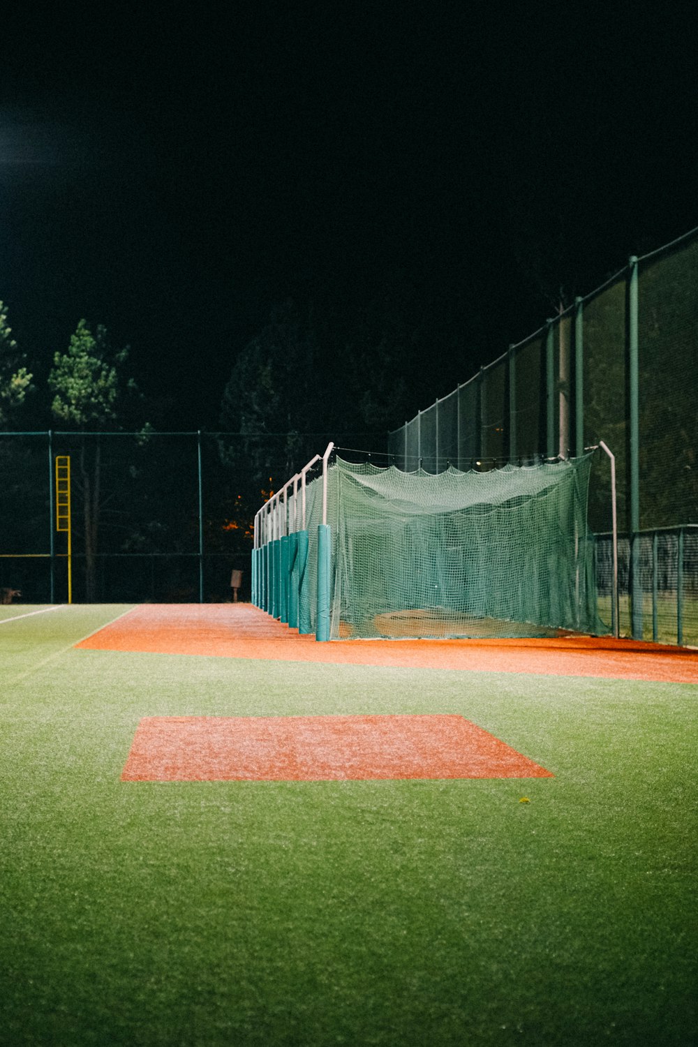 a baseball field at night with a batting cage