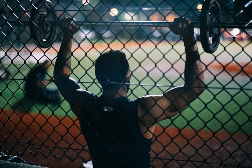 a man holding a barbell behind a fence