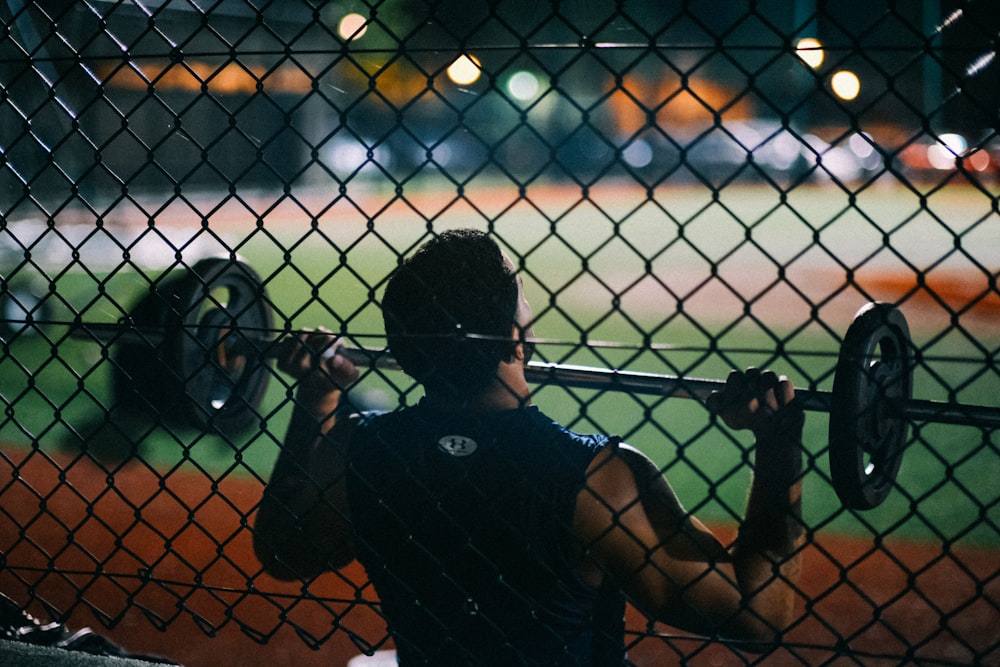 a man holding a barbell behind a fence