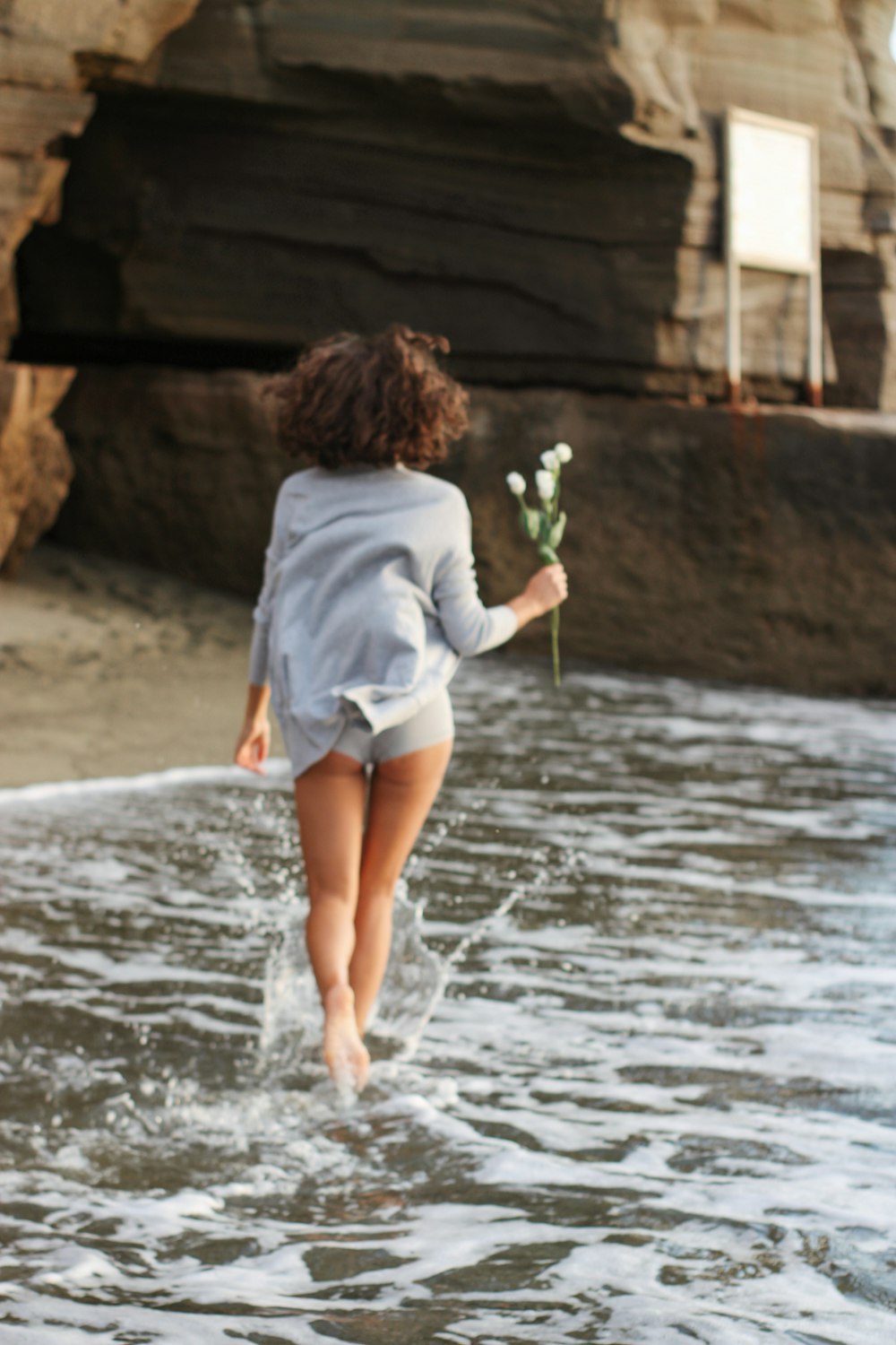 a young girl running into the ocean with a flower in her hand