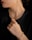 A person is wearing a gold chain necklace and matching bracelet. The individual is dressed in black, and the focus is on the luxurious jewelry. The hand is elegantly posed near the neck, highlighting both the bracelet and necklace.