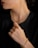A person is wearing a gold chain necklace and matching bracelet. The individual is dressed in black, and the focus is on the luxurious jewelry. The hand is elegantly posed near the neck, highlighting both the bracelet and necklace.