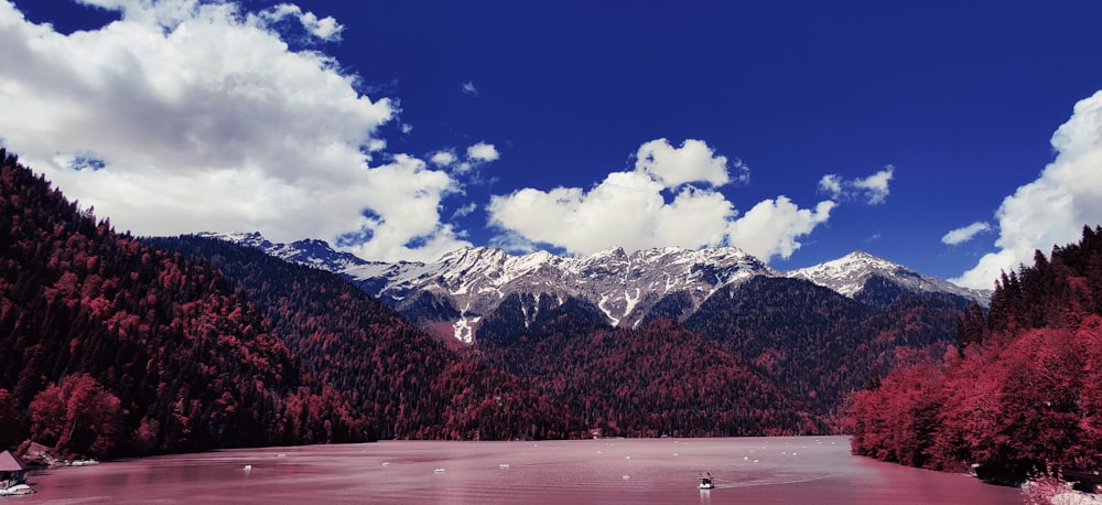 a lake surrounded by trees and mountains under a cloudy blue sky