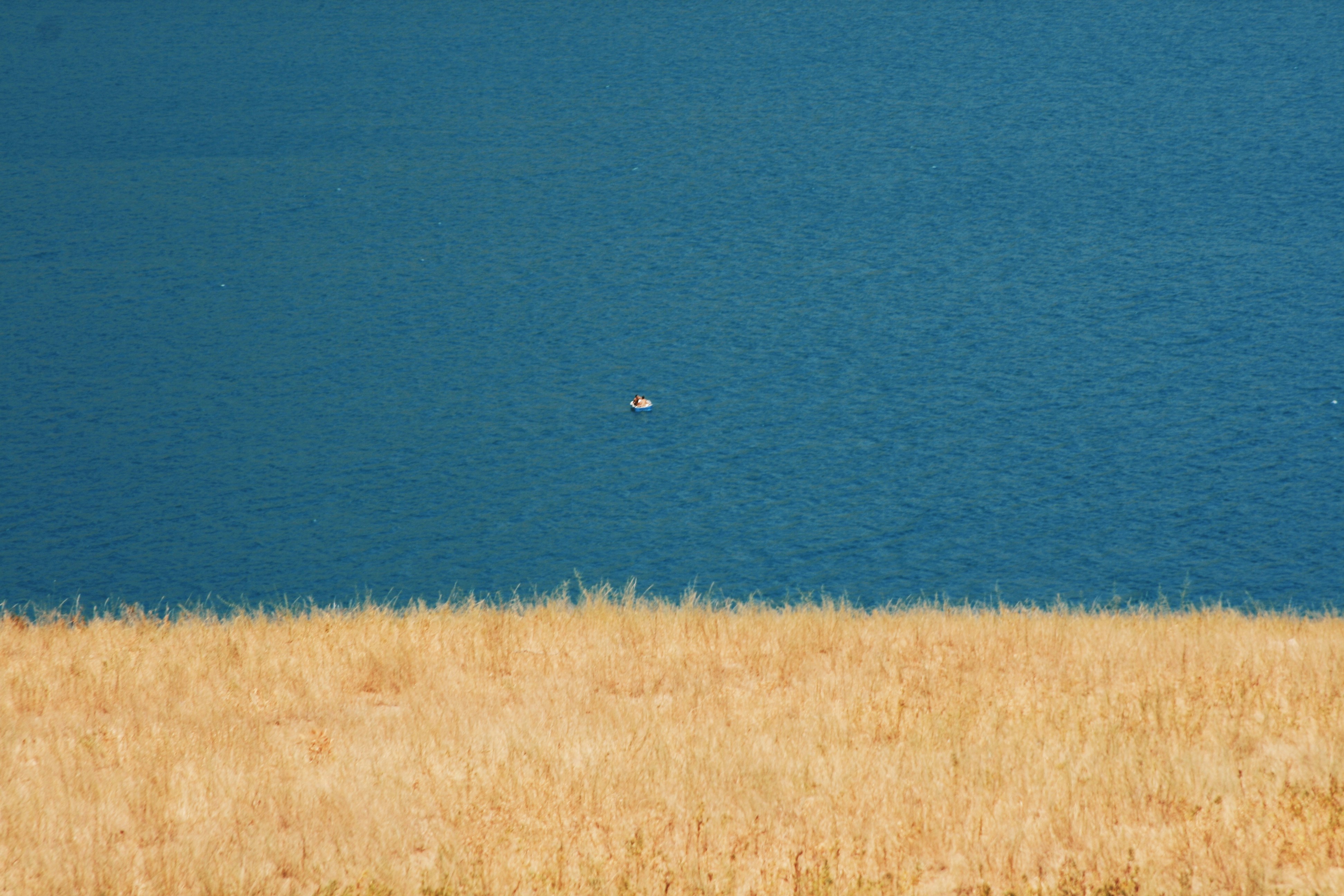 a large body of water sitting next to a dry grass field