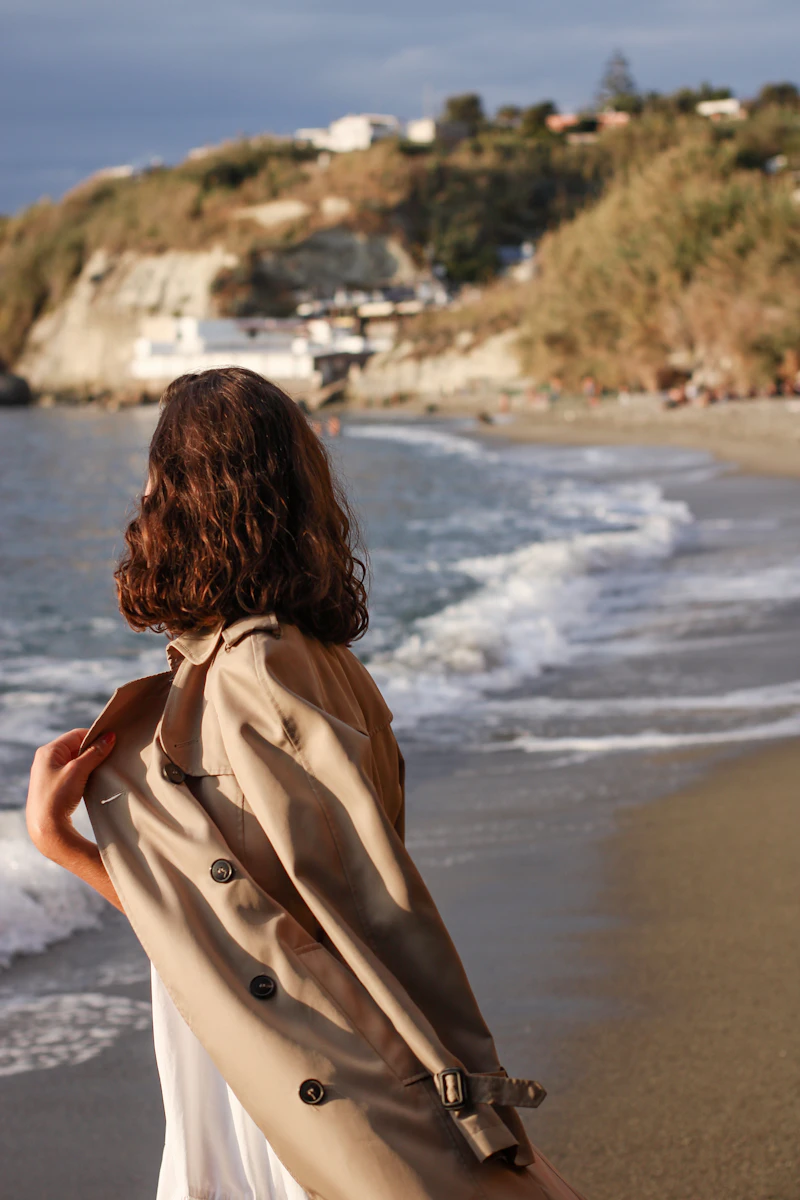 Woman in a beige cotton trench coat standing on the shoreline