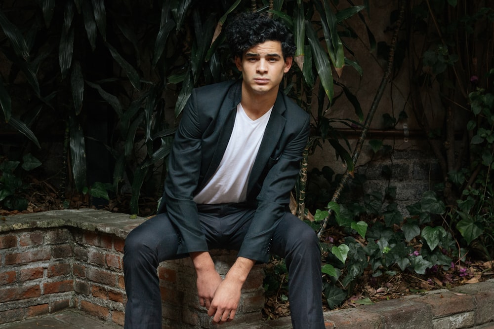 a man in a suit sitting on a brick wall