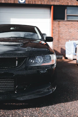 A sleek black car with a flawless finish parked in front of a modern garage.