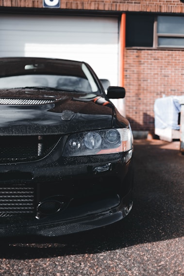 A shiny black sports car freshly detailed, glistening under the Wichita sun in front of a clean, modern garage.