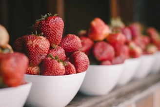 a row of white bowls filled with ripe strawberries