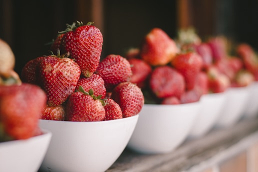 a row of white bowls filled with ripe strawberries