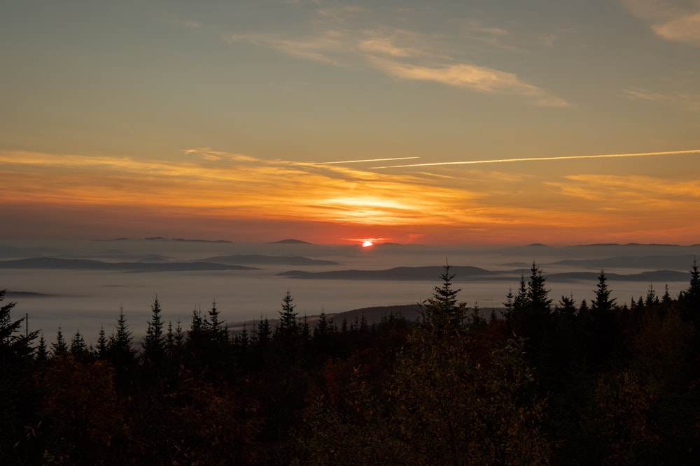 the sun is setting over the foggy mountains