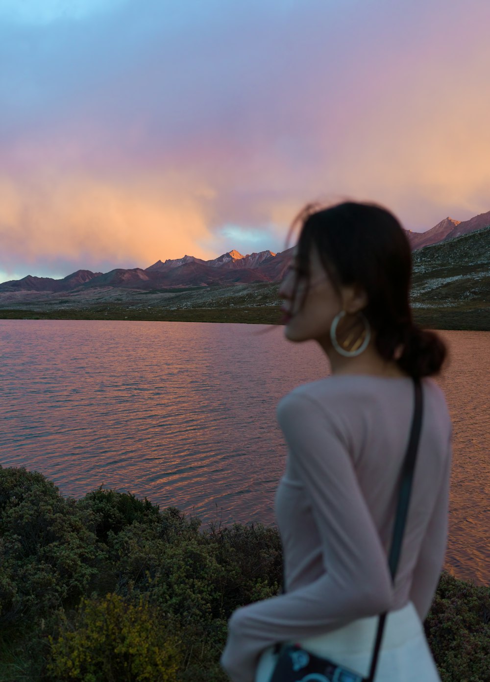 a woman is looking at the water at sunset